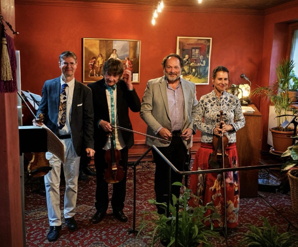 Die Mitwirkenden des 2. Atelierabends stehen nach der Aufführung im historischen Atelier der Sinne vor roten Lehmwänden und Gemälden.